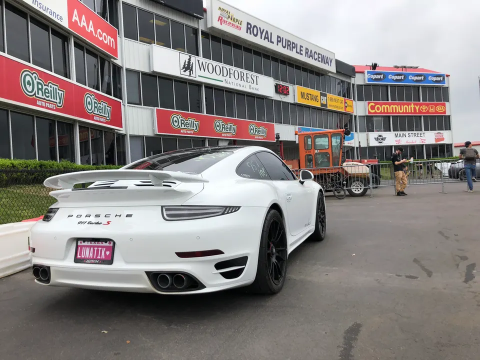 White Porsche 911 Turbo S with a large rear wing and quad exhaust tips parked at Royal Purple Raceway.