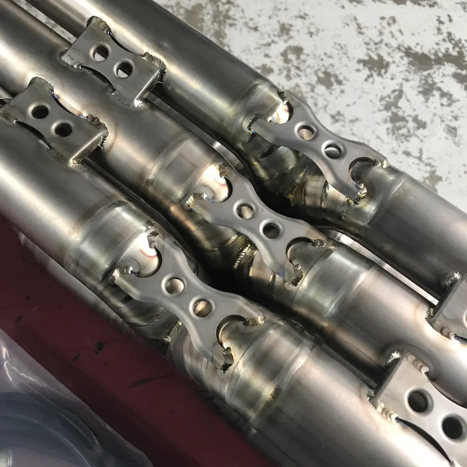 Close-up of custom fabricated stainless steel exhaust pipes with intricate welds and mounting brackets.