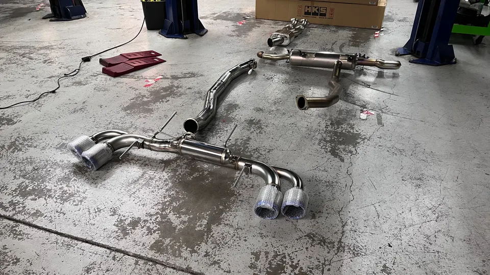 An HKS aftermarket exhaust system laid out on a concrete shop floor, ready for installation.