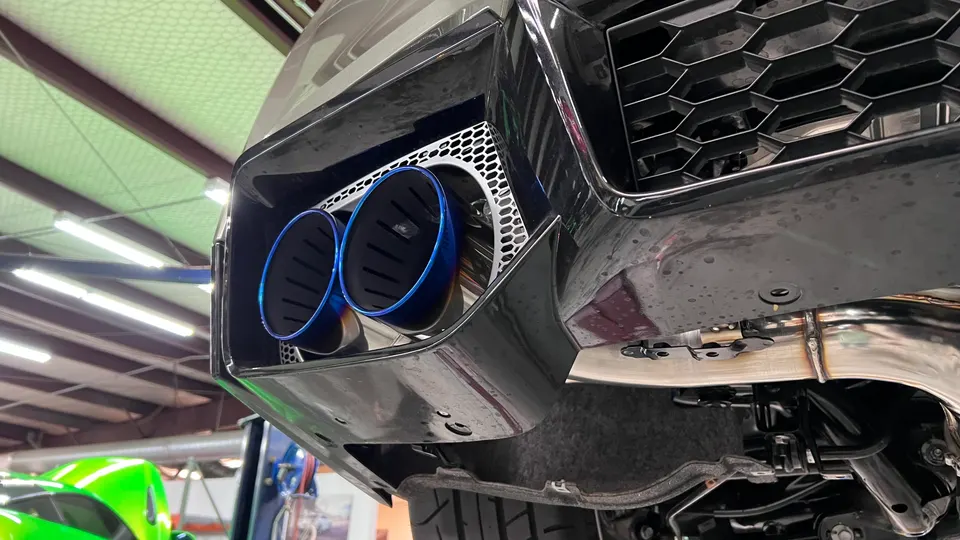 Close-up of blue titanium exhaust tips on a performance car, seen from the underside in a shop.