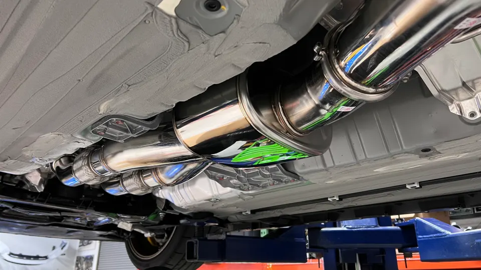 Undercarriage view of a car on a lift, showcasing a polished aftermarket exhaust system with a muffler.