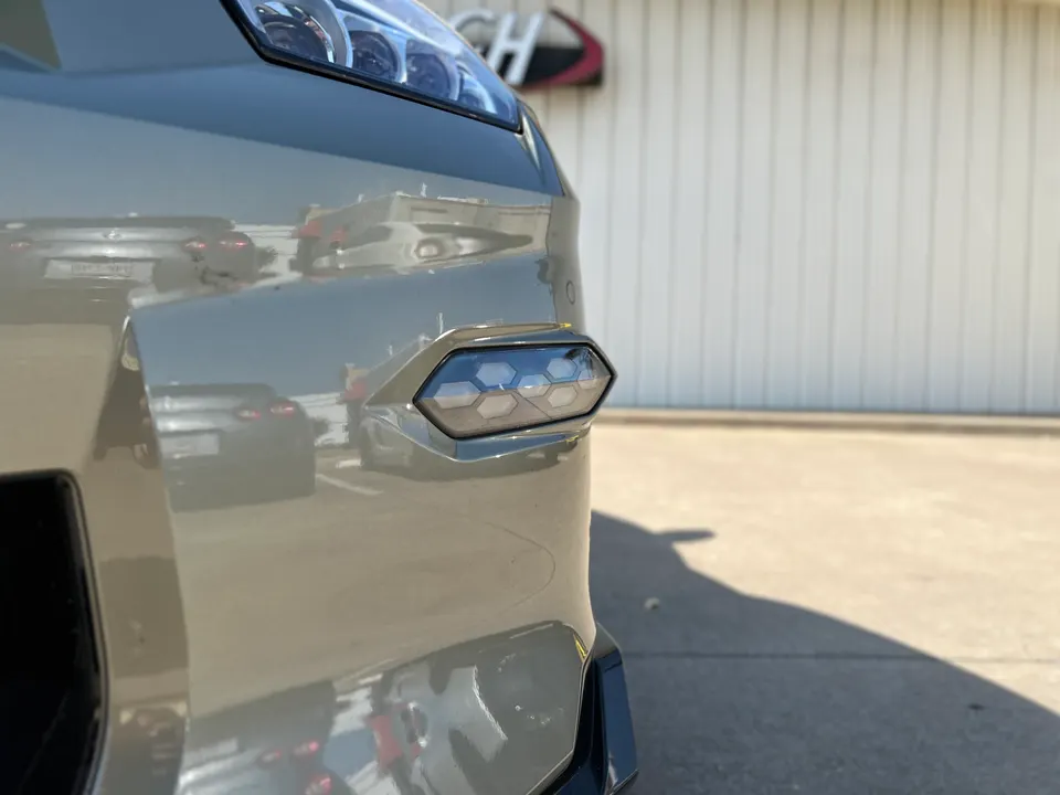 Close-up detail of a grey car's front bumper showing an aftermarket LED side marker light with a hexagonal pattern.