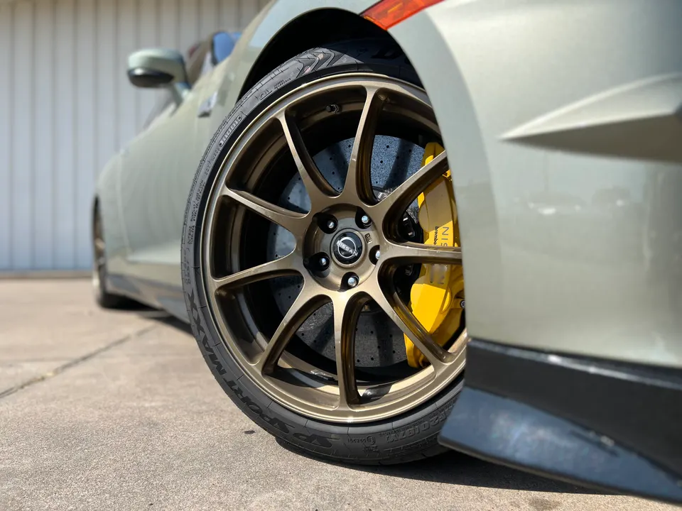 Close-up of a Nissan GT-R's bronze multi-spoke wheel with yellow Brembo calipers and Dunlop Sport Maxx tires.