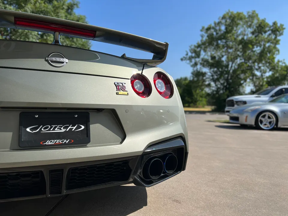 Rear view of a grey Nissan GT-R with Jotech license plate frame and aftermarket exhaust tips parked outdoors.