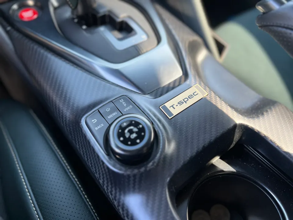 A close-up of a Nissan GT-R T-spec interior, showing the carbon fiber center console and infotainment controls.