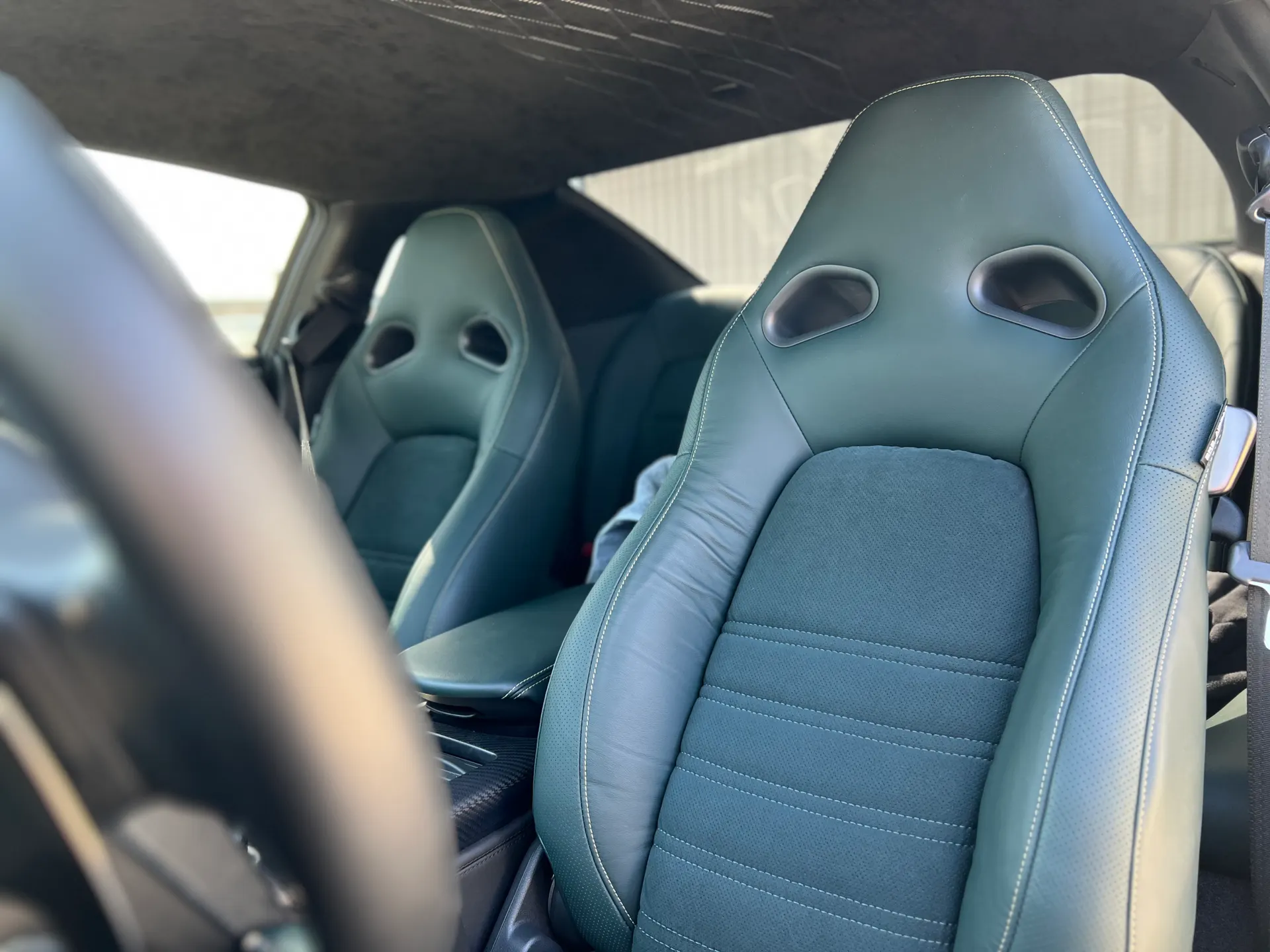Close-up of a custom car interior featuring green leather and fabric sport seats with white stitching.