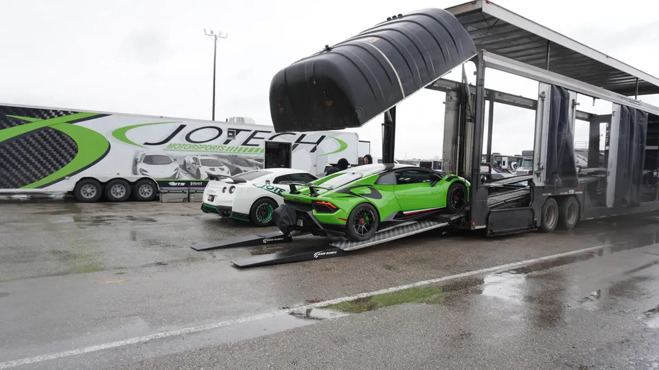 Green Lamborghini Huracan and white Nissan GT-R being unloaded from a Jotech Motorsports car hauler at a track event.