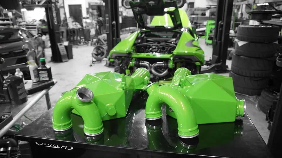 Bright green intercoolers and boost piping on a workbench in the Jotech Motorsports shop with a Lamborghini in the background