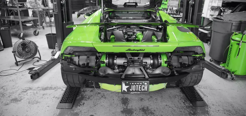 Green Lamborghini Huracan with exposed twin-turbo setup in a Jotech Motorsports shop, ready for tuning.