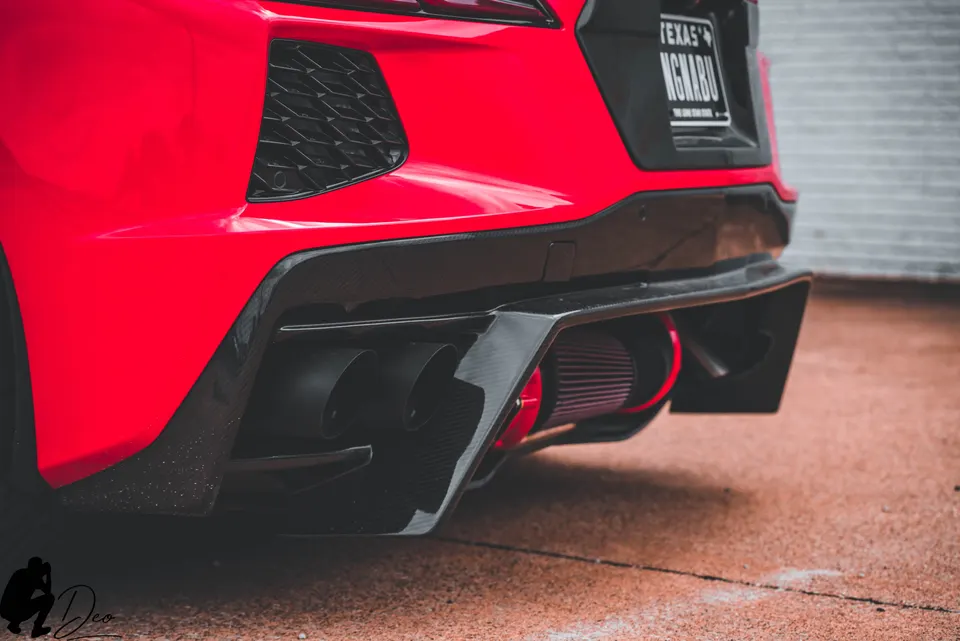 Rear detail of a red C8 Corvette featuring aftermarket exhaust tips, carbon fiber diffuser, and exposed performance air filter.
