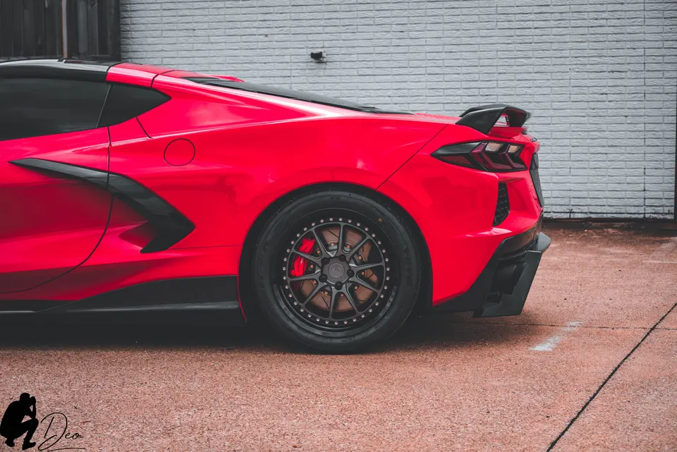A red Chevrolet Corvette C8 with custom black wheels, red brake calipers, a black rear spoiler, and a black rear diffuser.