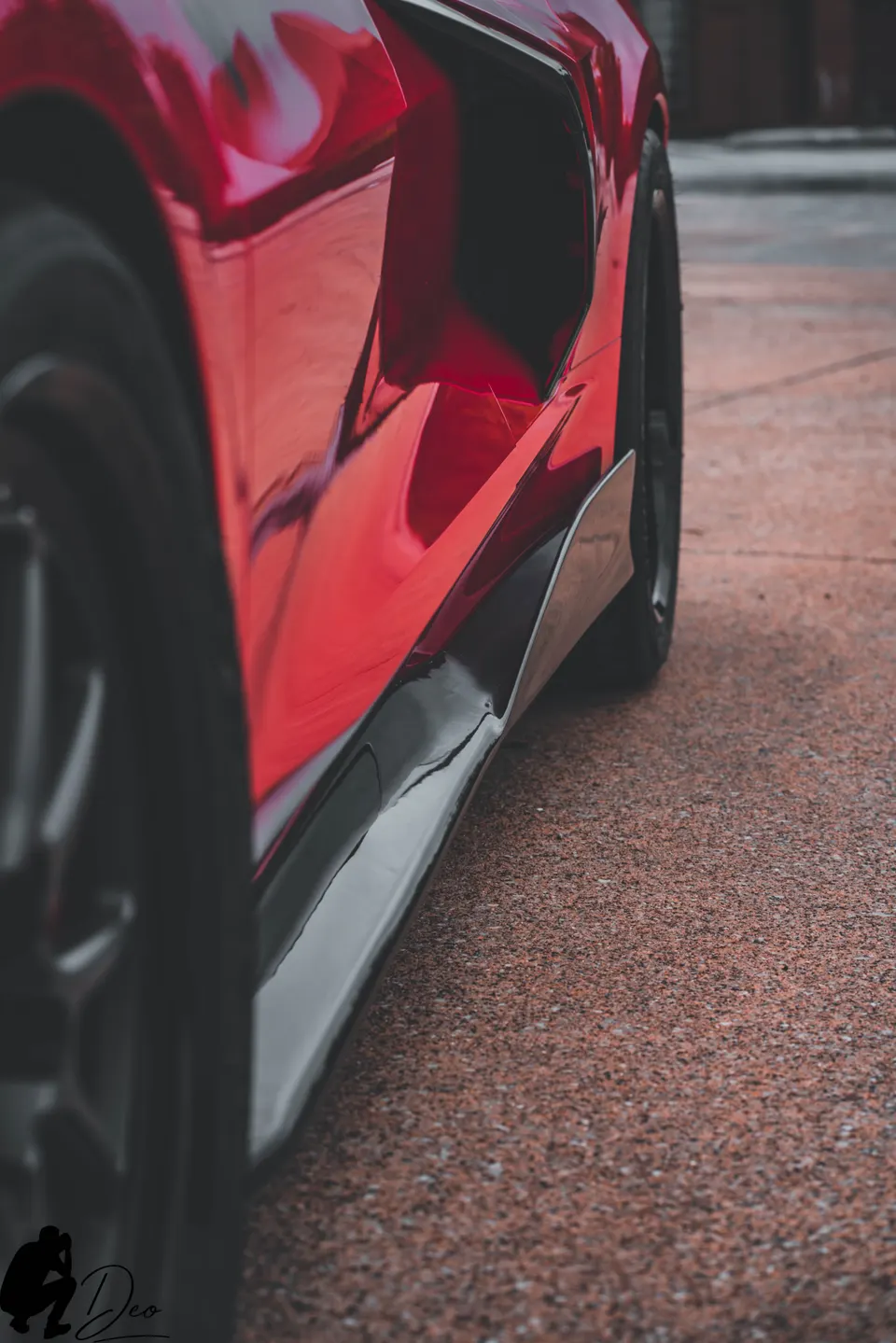A close-up of the glossy red side and black side skirt of a C8 Corvette, showcasing its aerodynamic design.