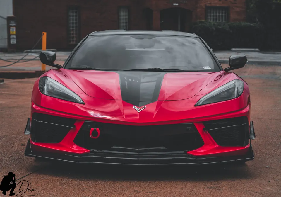 Front view of a red Corvette C8 with a black racing stripe, front splitter, and red tow hook.