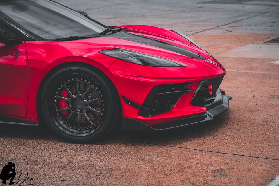 Red C8 Corvette with aftermarket wheels, red brake calipers, and a black front splitter parked on asphalt.