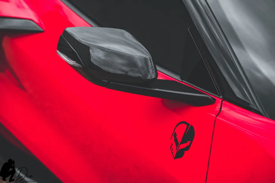 Close-up of a red Corvette's carbon fiber side mirror and C8 logo on the door.