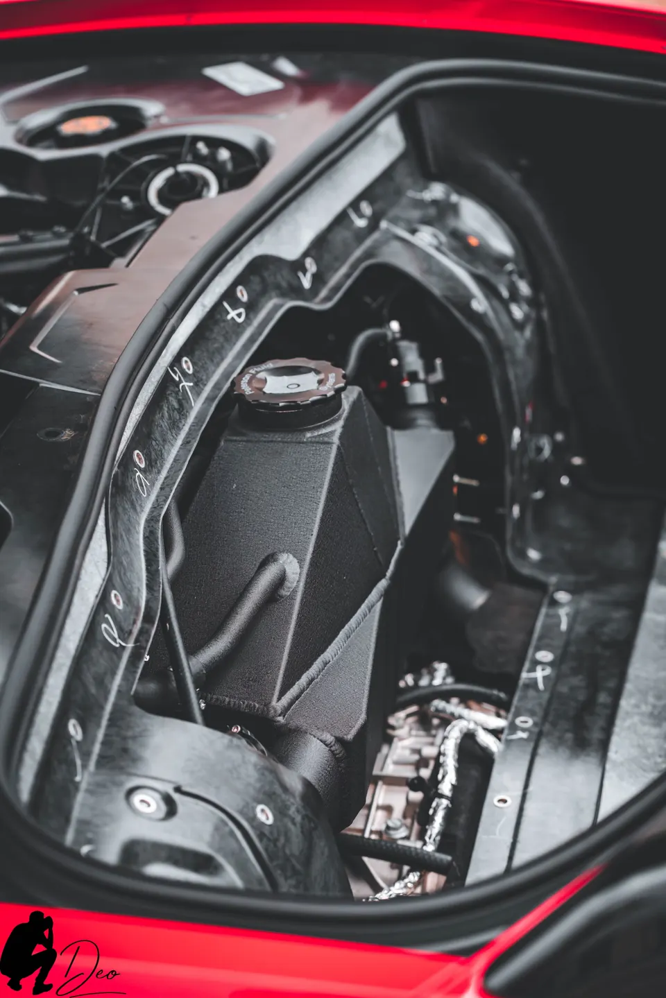 Close-up of an aftermarket coolant reservoir in the engine bay of a red performance car.