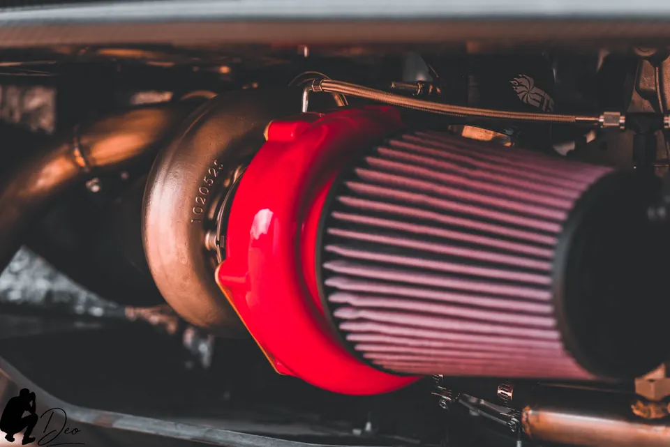 Close-up shot of a performance turbocharger with a red air filter installed in an engine bay.