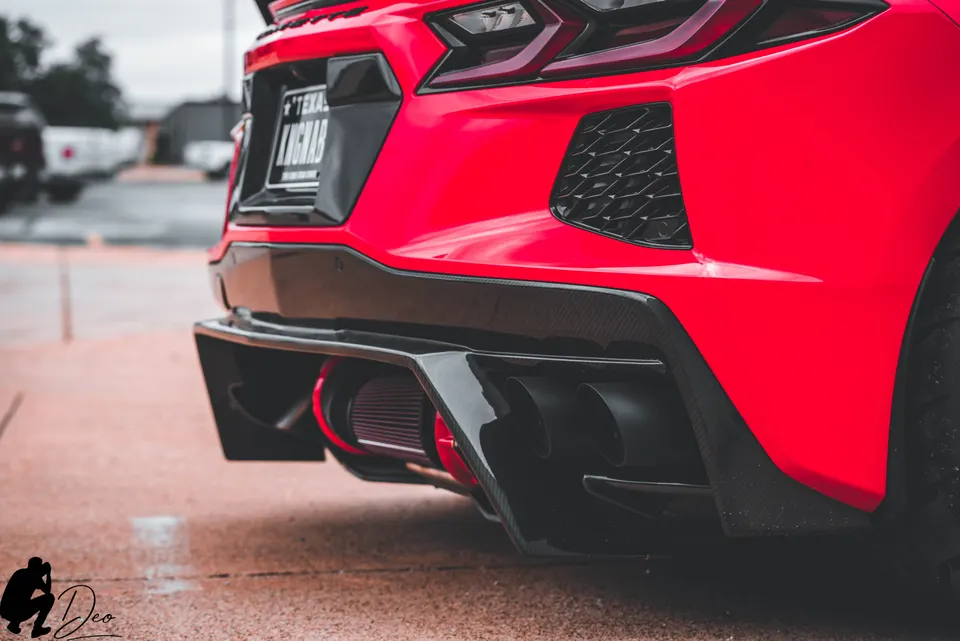 Rear view of a red C8 Corvette with a carbon fiber diffuser, aftermarket exhaust tips, and a visible red air filter.