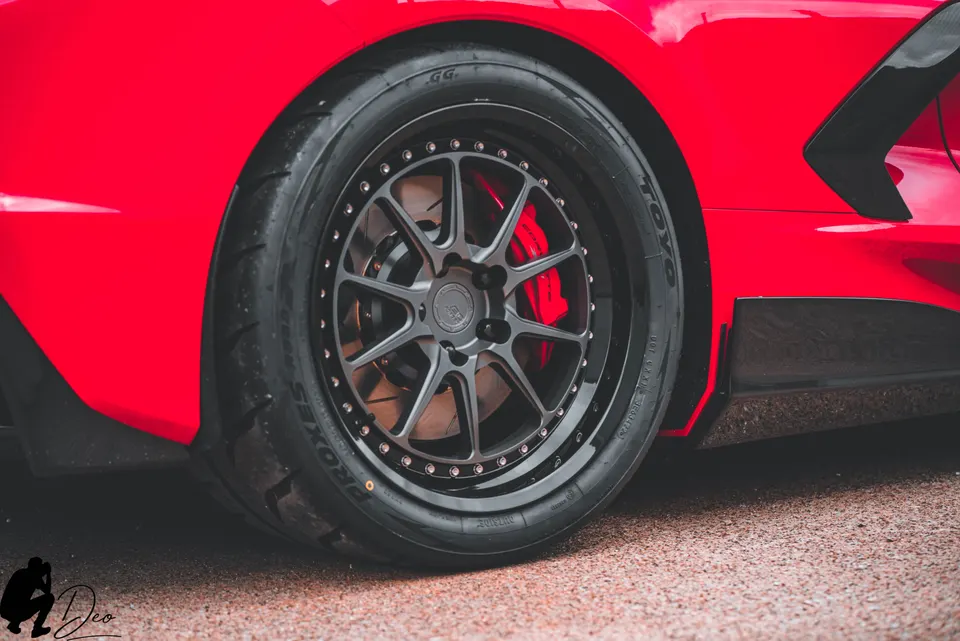 Close-up of a red sports car's custom black multi-spoke wheel, performance tire, and red brake caliper.