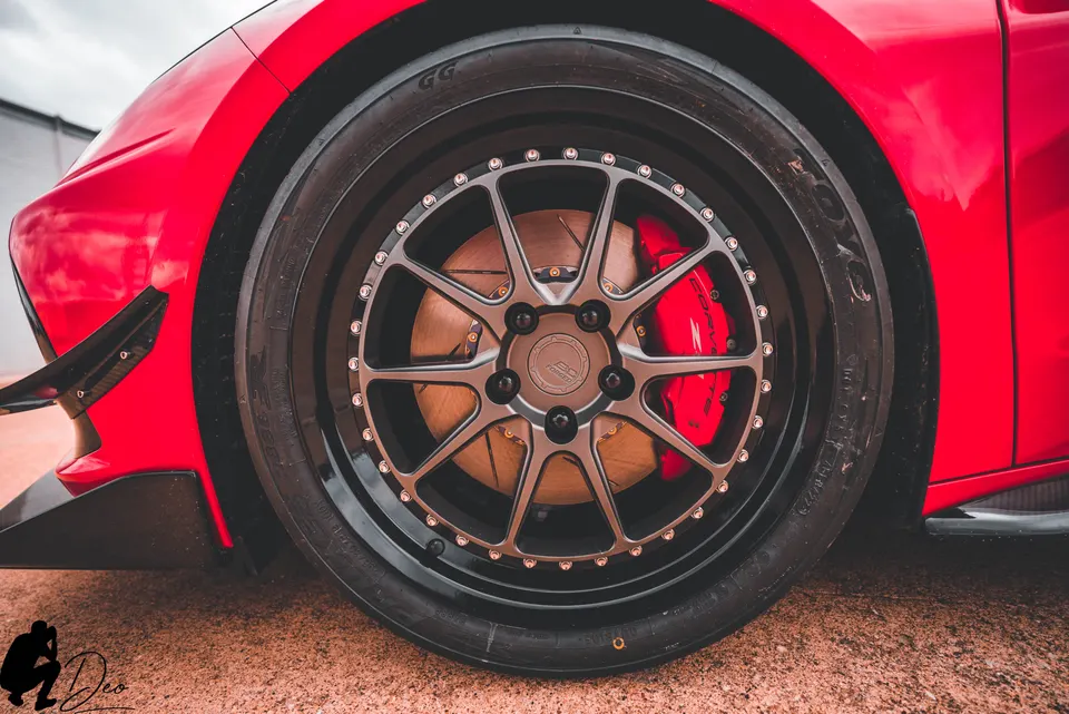 A close-up of a red car's custom BC Forged wheel with a red brake caliper and performance tire.