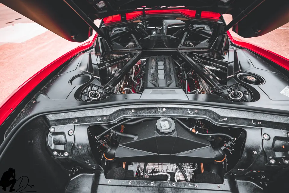 Overhead view of a red Chevrolet Corvette C8 mid-engine bay with the engine cover open, showcasing the V8 engine.