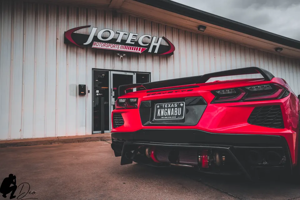 Rear view of a red C8 Corvette with visible twin turbo setup, parked outside Jotech Motorsports.