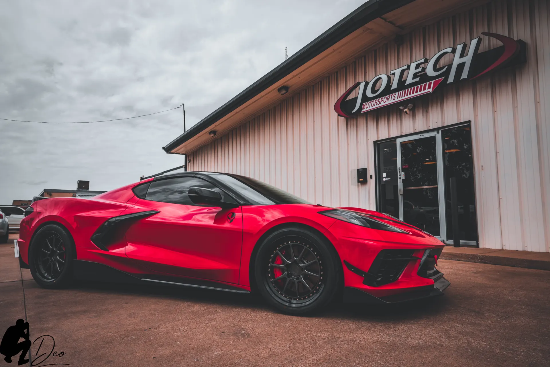 A red Corvette C8 with aftermarket wheels and aero parked outside Jotech Motorsports performance shop.