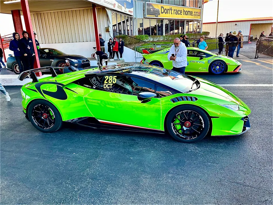 Bright green Lamborghini Huracan with a large rear wing at a drag strip, with another green Lamborghini in the background.