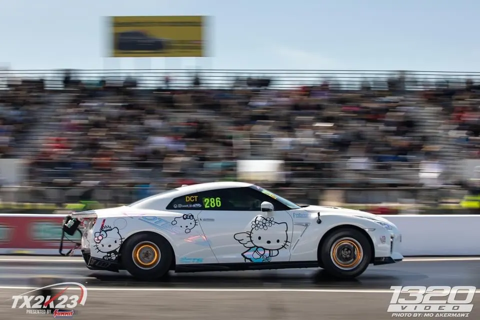 White Nissan GT-R with Hello Kitty livery accelerating down a drag strip during the TX2K23 event.