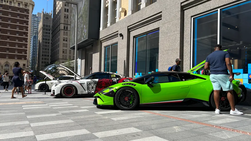 Modified Lamborghini Huracan and Nissan GT-R parked on a city street during a car show with people admiring them.