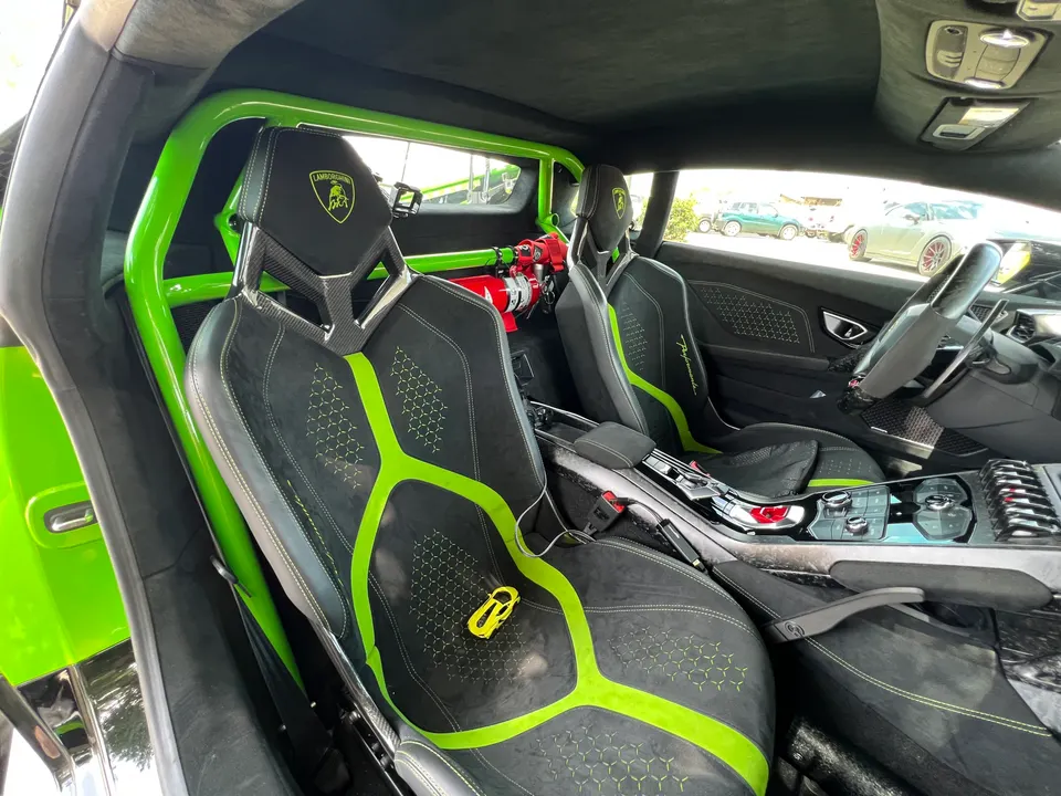 Interior view of a Lamborghini with a bright green roll cage, racing seats with green accents, and a fire extinguisher.