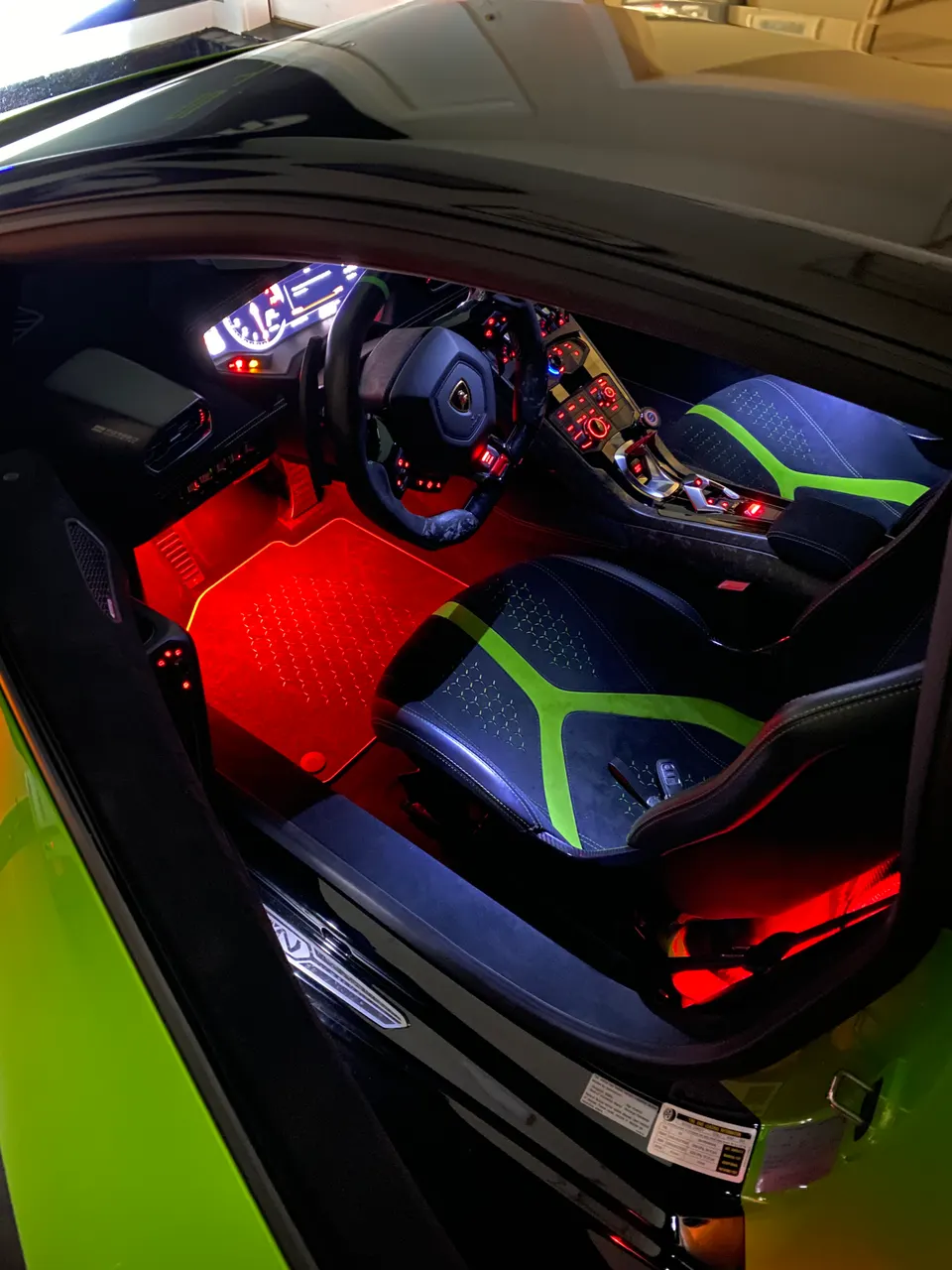 Detailed view of a Lamborghini interior featuring custom black and green seats, red ambient lighting, and a sporty steering wheel.