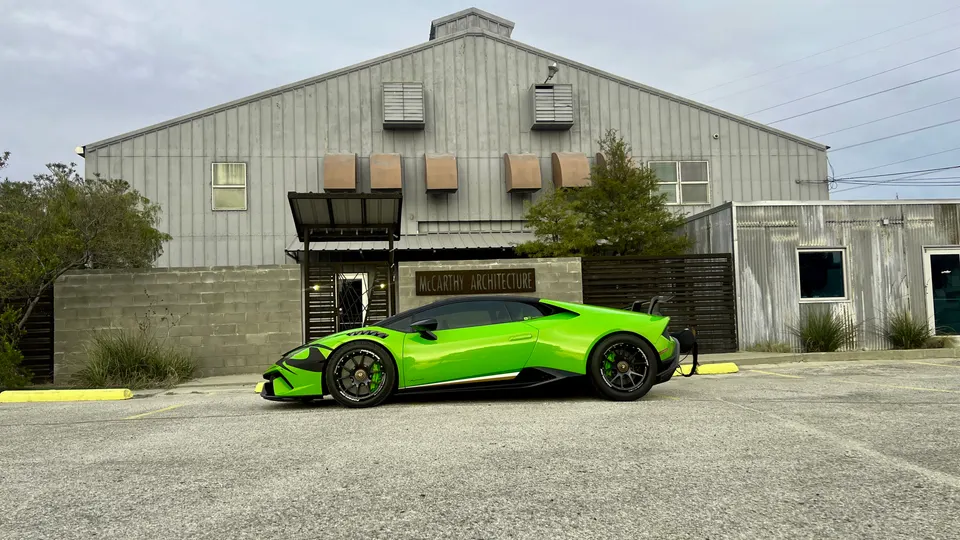 A vibrant green Lamborghini Huracan with custom wheels and aftermarket aero parked in front of a modern industrial building.