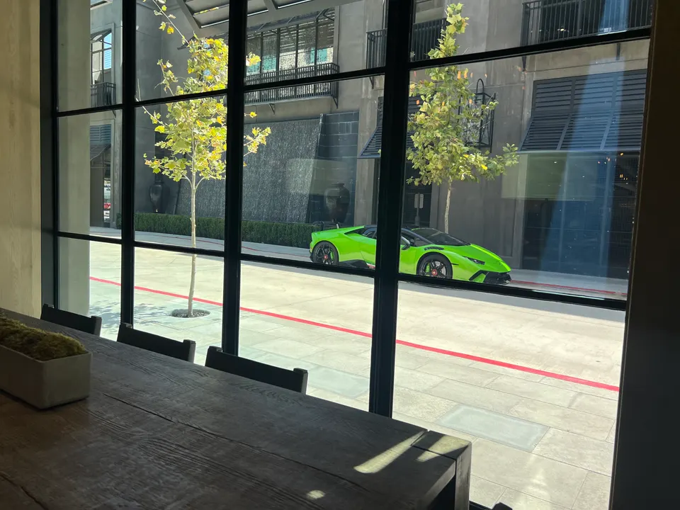 A bright green Lamborghini Huracan parked outside a modern building, viewed through a large window from an interior setting.