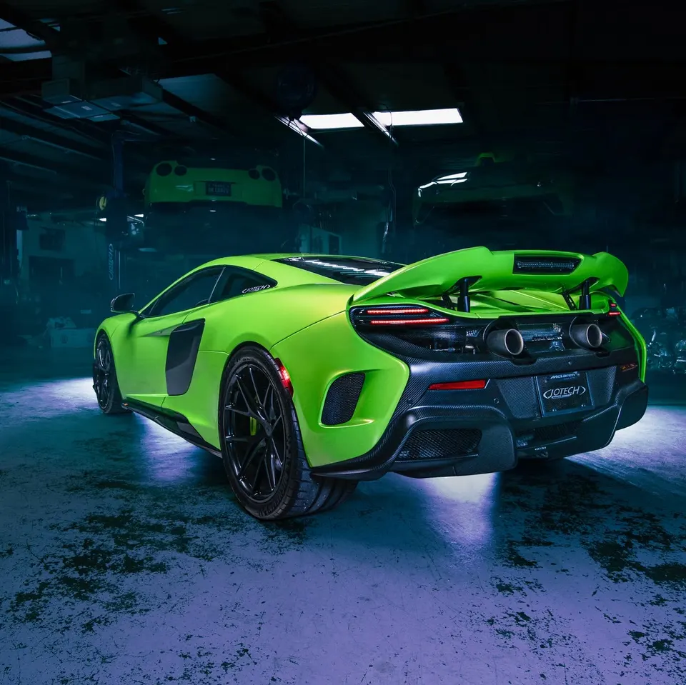 Bright green McLaren supercar with a large rear wing and carbon fiber diffuser in a performance shop.