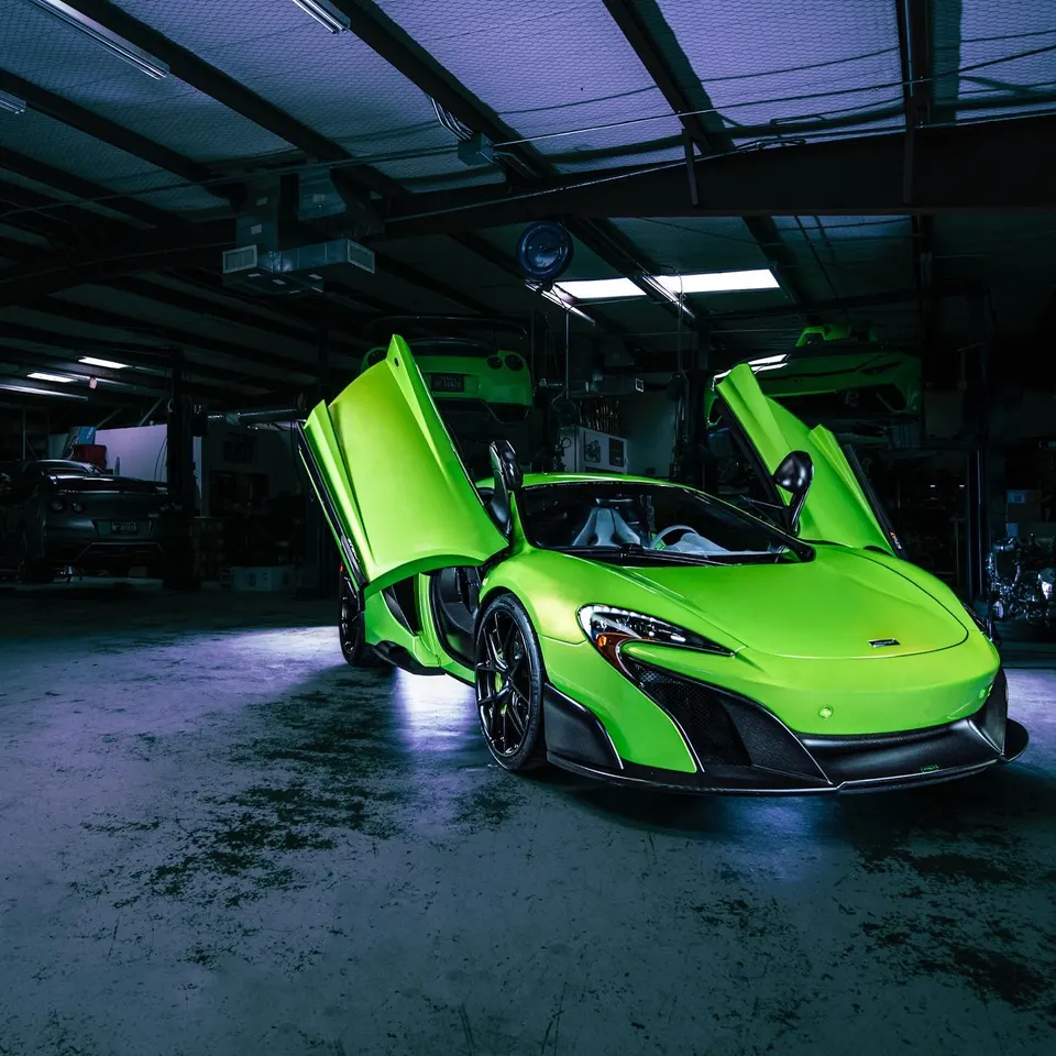 A bright green McLaren 650S supercar with butterfly doors open, parked in a performance tuning shop.