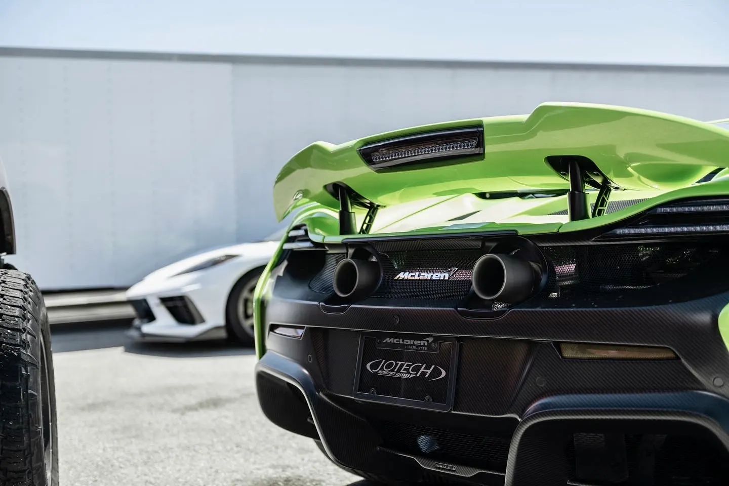 Rear view of a vibrant green McLaren supercar, highlighting its carbon fiber rear wing, aggressive diffuser, and dual exhaust tips.