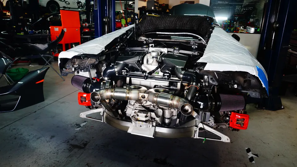A McLaren supercar undergoing a performance build in a shop, with its twin-turbo engine and custom exhaust system exposed.
