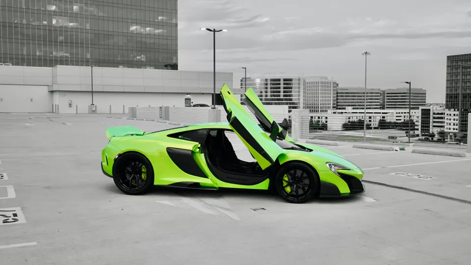 Lime green McLaren supercar with butterfly doors open, parked on a rooftop parking lot with a city skyline in the background.