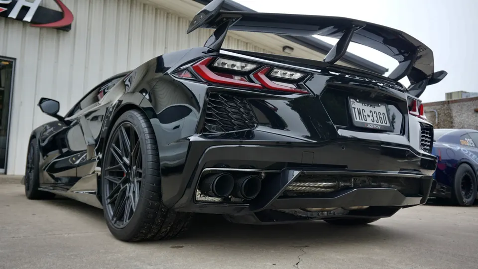 A black Corvette C8.R with a large rear wing, aggressive diffuser, and quad exhaust parked outside Jotech Motorsports.