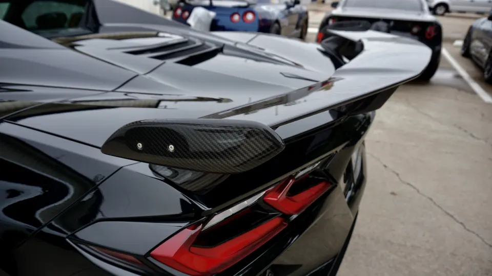 A close-up of the rear of a black Chevrolet Corvette C8, highlighting the carbon fiber rear wing and LED taillights.