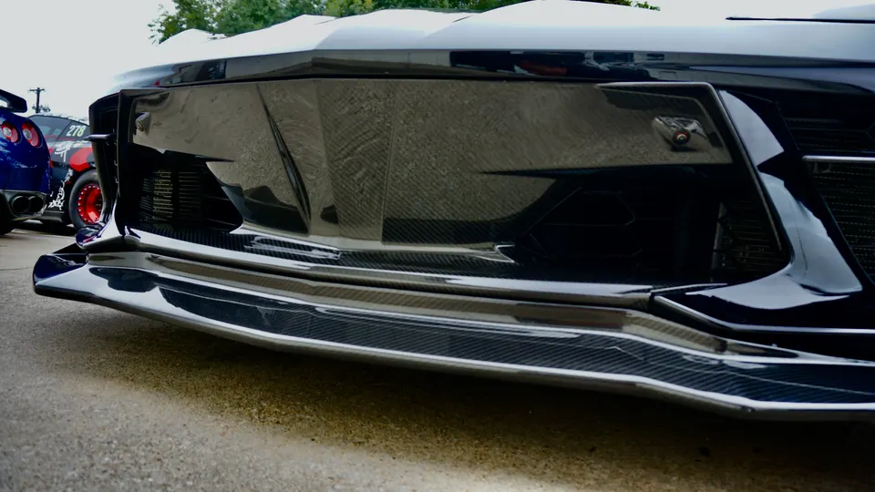 Close-up of a performance car's front bumper and carbon fiber splitter, showcasing custom aerodynamic modifications.
