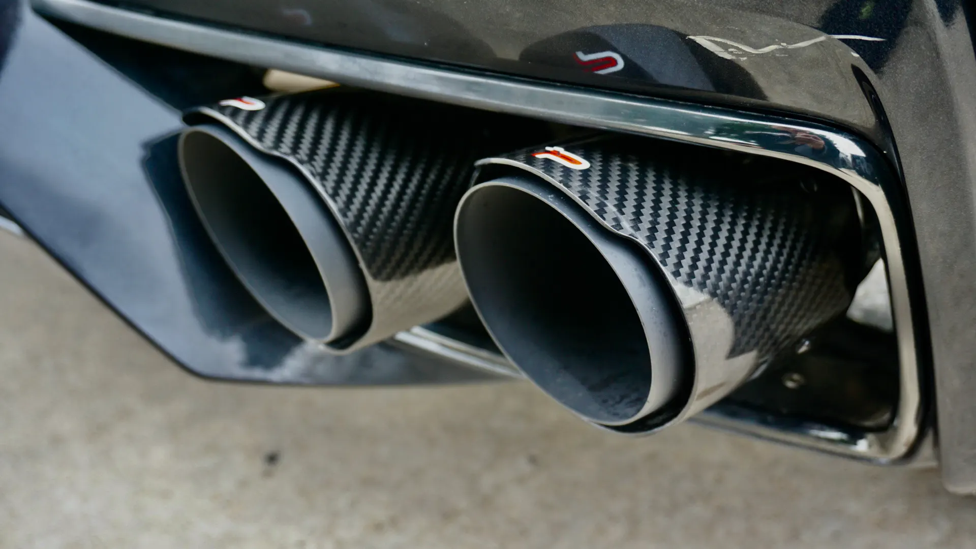 Close-up of a car's dual carbon fiber exhaust tips integrated into the rear bumper.