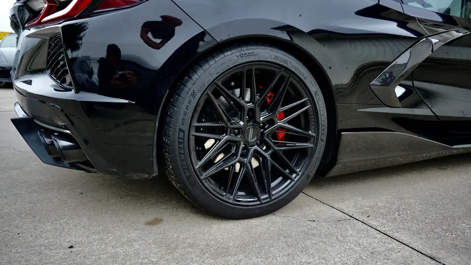 Rear quarter view of a black Corvette C8 with custom black wheels, red brake calipers, and carbon fiber aero.