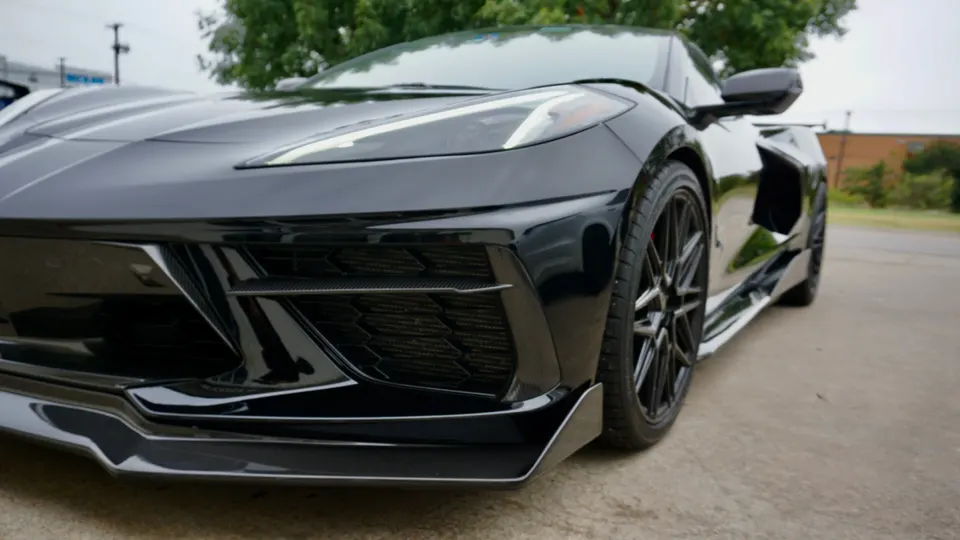 A black C8 Corvette with an aftermarket front splitter and side skirts parked outdoors.