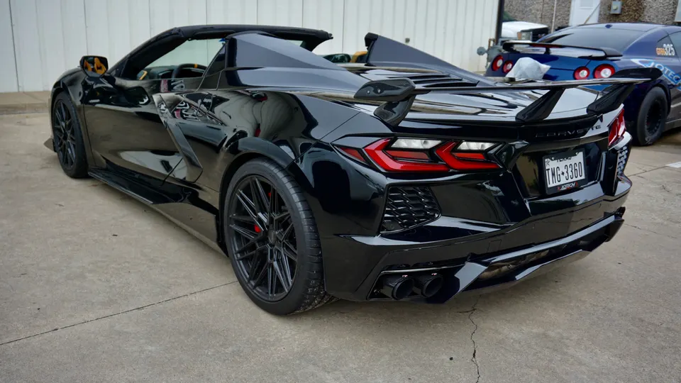 Black Chevrolet Corvette C8 convertible with aftermarket wheels, rear wing, and custom exhaust tips, parked next to a blue Nissan GT-R.
