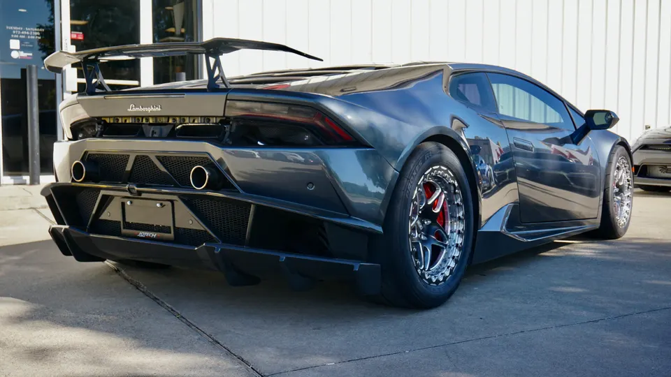 A grey Lamborghini Huracan with a large rear wing, aggressive diffuser, and aftermarket wheels parked outside a shop.