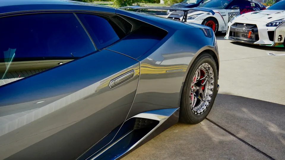 Grey Lamborghini Huracan with custom drag wheels and red calipers parked at an outdoor event with other modified cars.