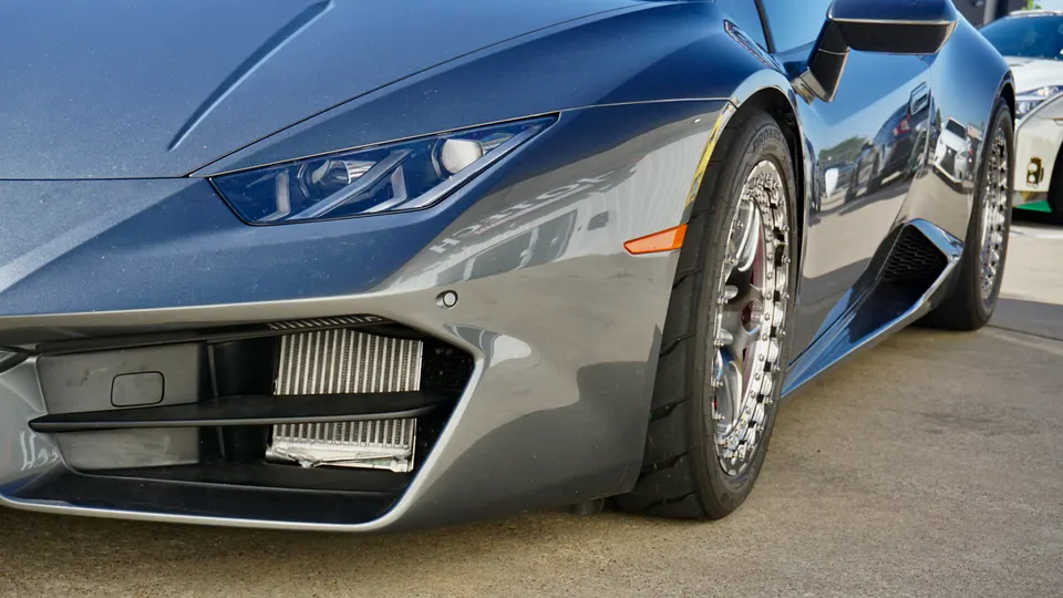 Close-up of a grey Lamborghini Huracan's front bumper, showcasing an aftermarket intercooler and custom wheels.