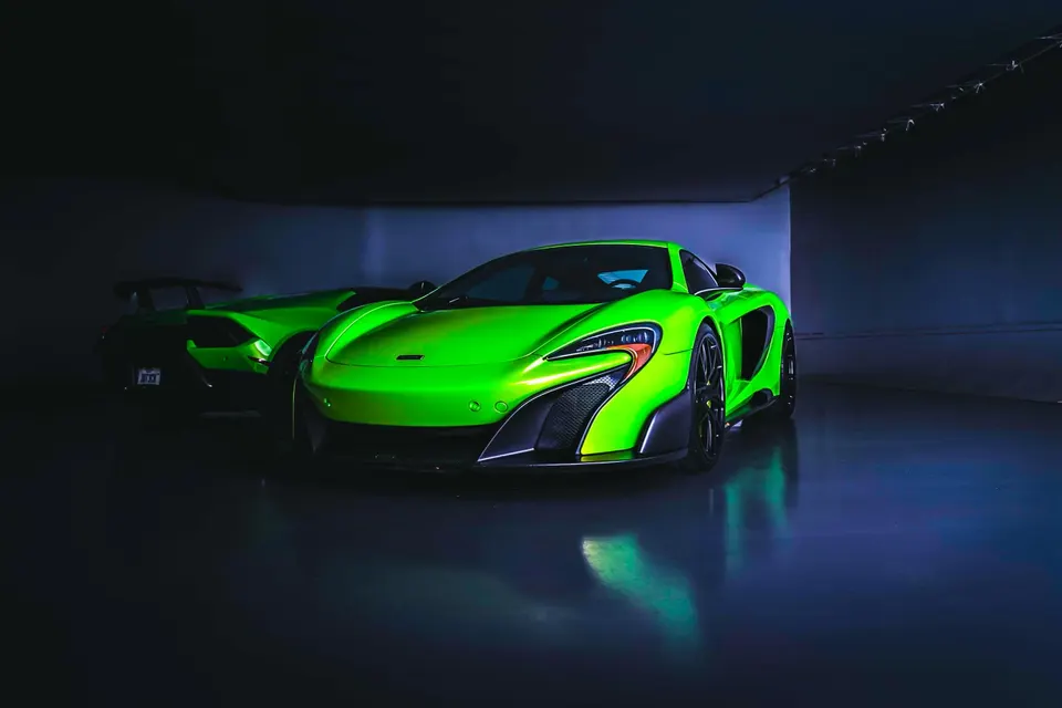 A bright green McLaren supercar parked in a dark, moody setting with another green car in the background.
